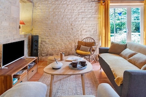 A cozy living room with a stone wall, a flat-screen TV, a wooden coffee table, and a comfortable sofa. - Gîte le Gué de Champagné, 10 min from St Jean d'Angély, 400 m from La Boutonne River (Torxé)