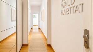 Un couloir doté d’un plancher en bois, de murs blancs et d’une porte sur laquelle on peut lire l’inscription « SCHWALD HABITAT ».