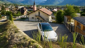 Un coche blanco estacionado en un área de grava con una iglesia y montañas al fondo.