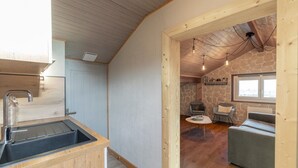 Una cocina con un lavamanos y encimera de madera, pared de piedra, techo de piedra y un rincón de estar con una mesa y sillas.