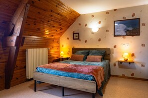 Une chambre avec un plafond en bois, un lit recouvert de plusieurs oreillers, deux lampes de chevet, un tableau encadré accroché au mur et une petite étagère sur laquelle se trouve une lampe.