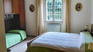 Et soveværelse med seng, natbord, et vindue med gardiner og en radiator.