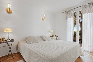 A bedroom with a bed, bedside lamps, a nightstand, and a view through a window with curtains. - Cosy Apartment 'Le Mas Du Soleil' with Sea View, Wi-Fi and Air Conditioning (Sainte-Maxime)