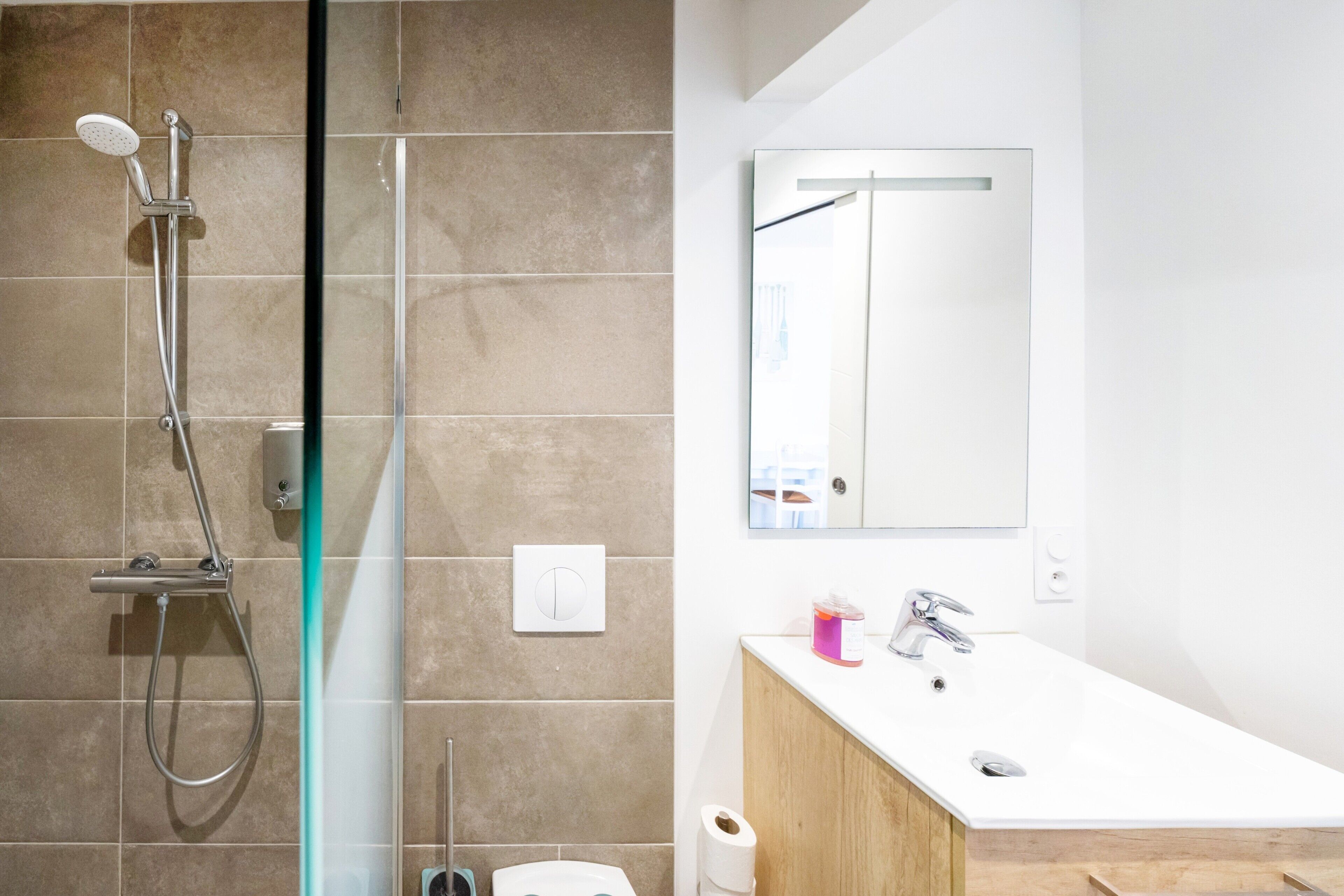 Une salle de bain avec une douche à parois de verre, un lavabo blanc avec un meuble en bois, et un miroir au-dessus du lavabo.