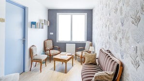 Een kamer met een blauwe deur, een groot raam, een gestreept sofa en een boekenplank.