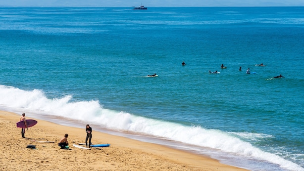 Een strand met surfers en een schip in de verte.