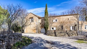 Un edificio de piedra con camino de grava, cerca de madera y un árbol alto.