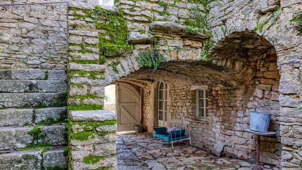 Un patio de piedra con un banco, una mesa de metal con un cubo y una puerta que da a otra habitación.