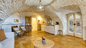 Un interior rústico con paredes de piedra, chimenea, mobiliario de mimbre y una mesa redonda.