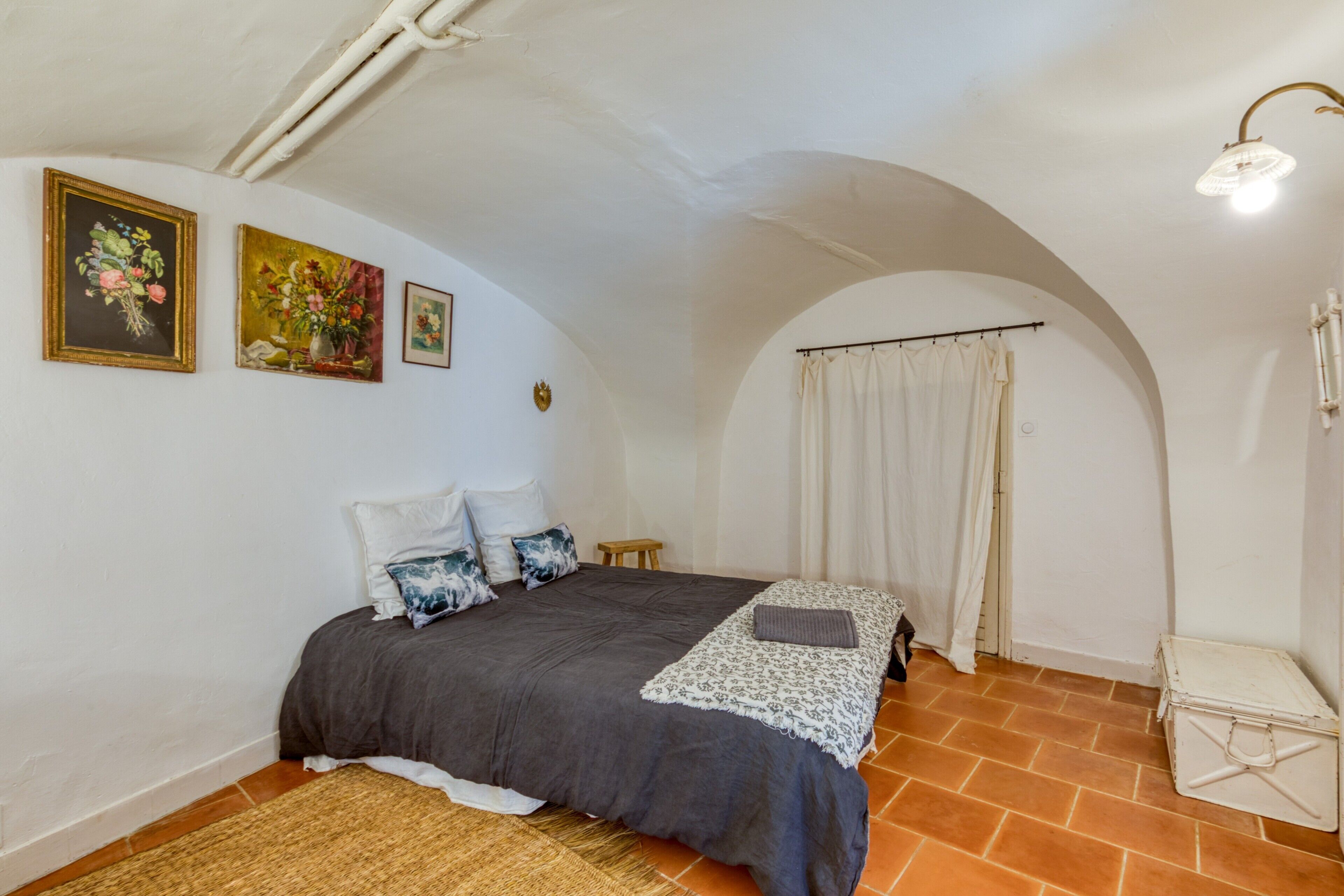 Un dormitorio con una cama, una mesita, una maleta y una pared con tres cuadros.
