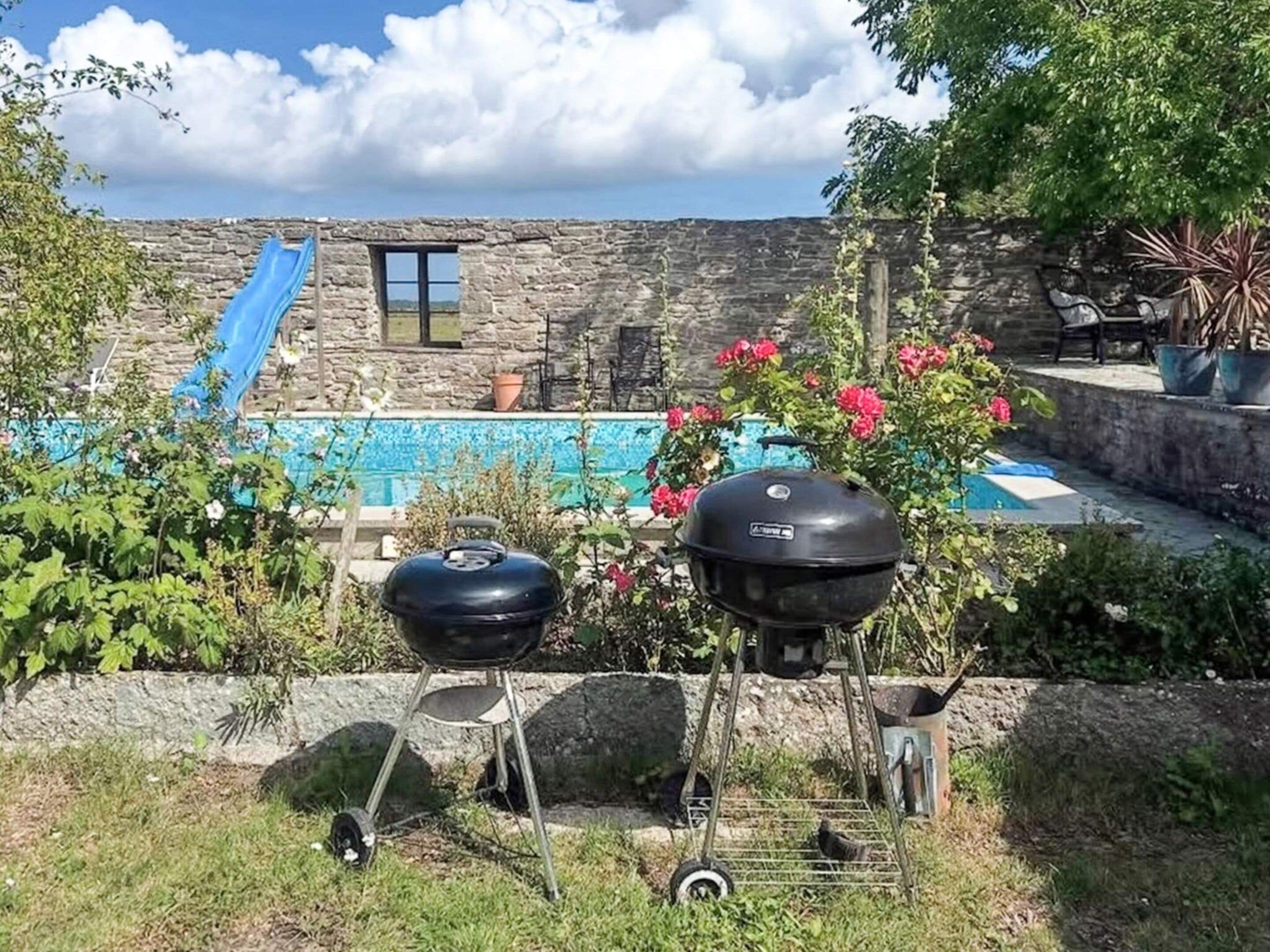 Un jardin avec un mur en pierre, un toboggan bleu, un barbecue et une piscine.