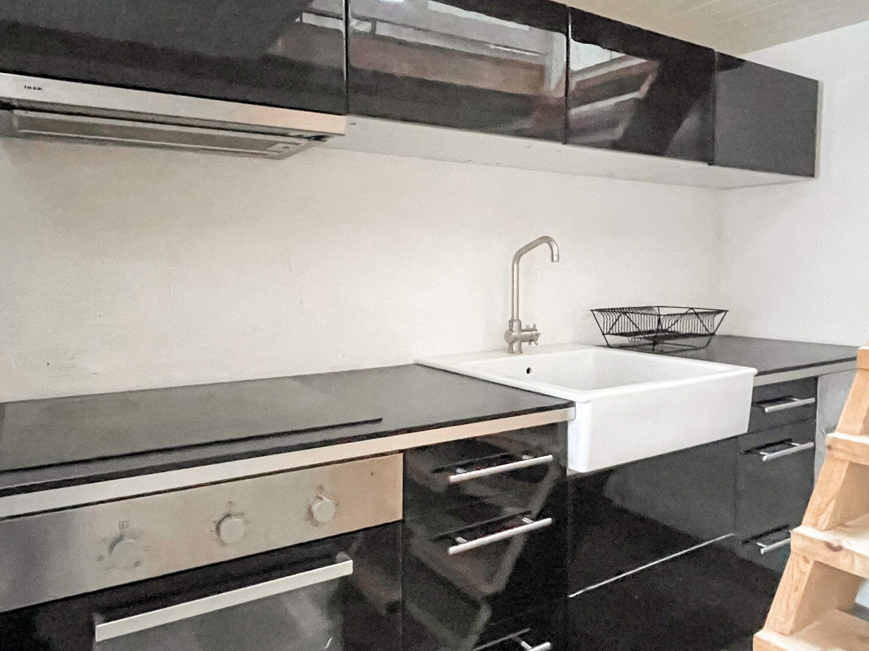 Een keuken met zwarte kastjes, een witte spoelbak en een roestvrijstalen afzuigkap.