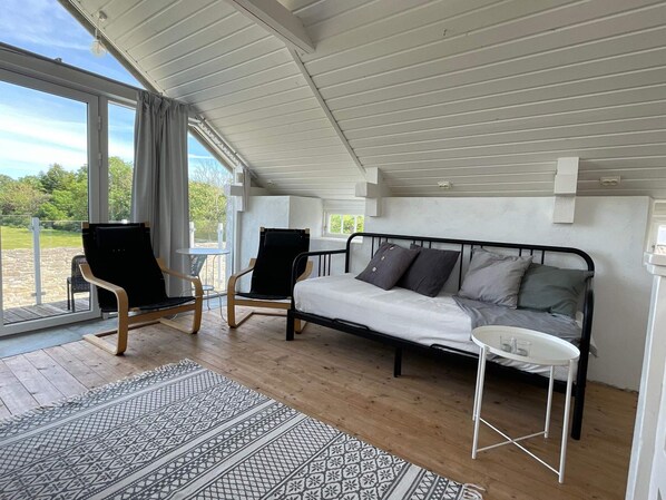 Une chambre avec un lit, deux chaises, une petite table et une vue sur l’extérieur.