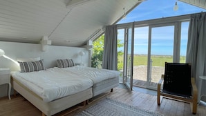 A bedroom with a large bed, a small table, a standing lamp, and a view of the outdoors. - 4 Person Holiday Home in Morbylanga (Morbylanga)
