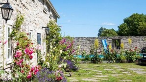 A stone building with a garden featuring various flowers and a stone pathway. - 4 Person Holiday Home in Morbylanga (Morbylanga)