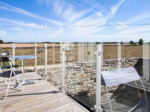 Eine Holzterrasse mit Glasverkleidung, einem Metallstuhl und einem Tisch.