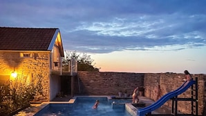 A swimming pool with a slide, stone walls, and a building with a tiled roof. - 4 Person Holiday Home in Morbylanga (Morbylanga)