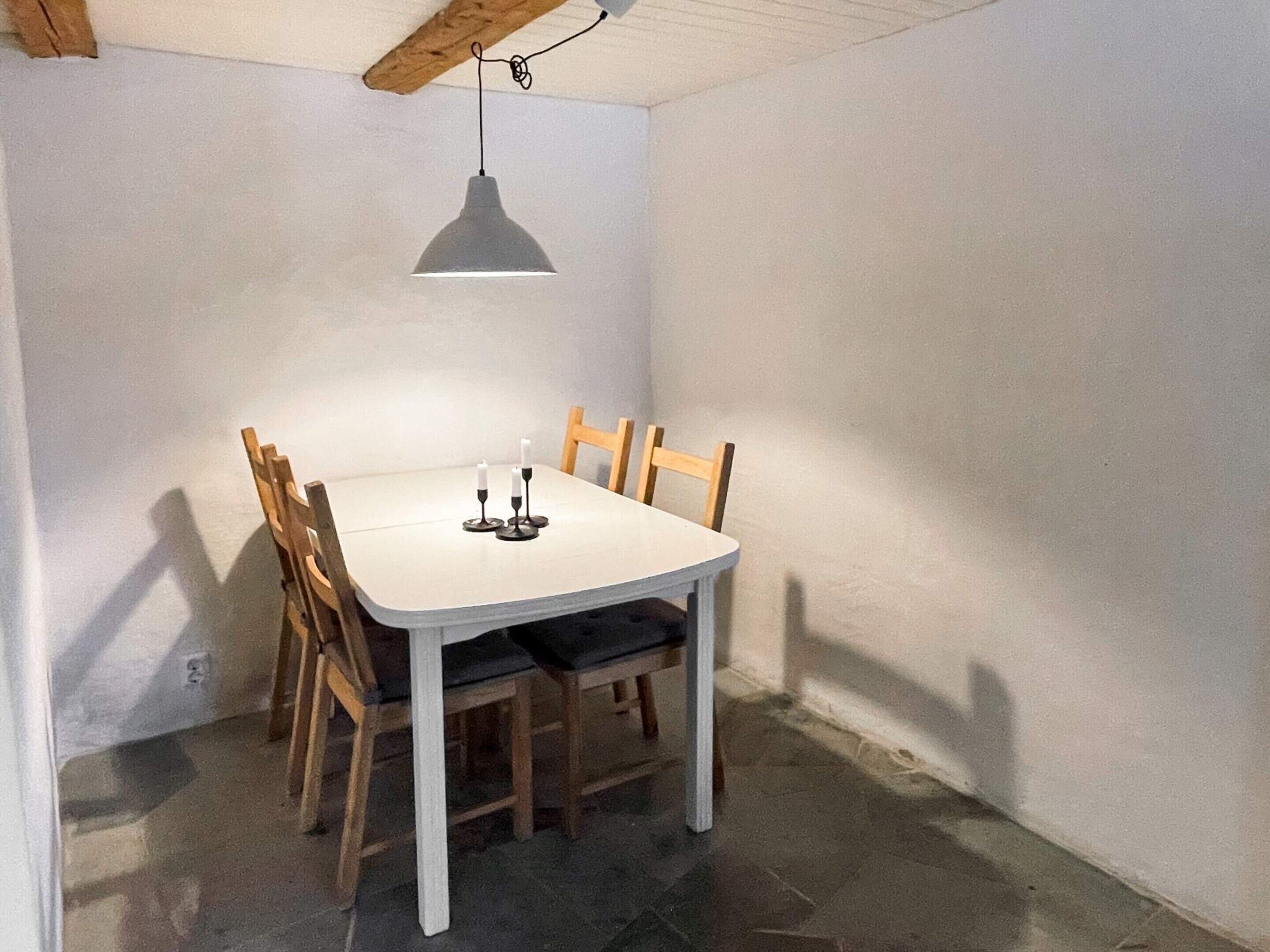 A dining area with a white table, four wooden chairs, and a pendant light.