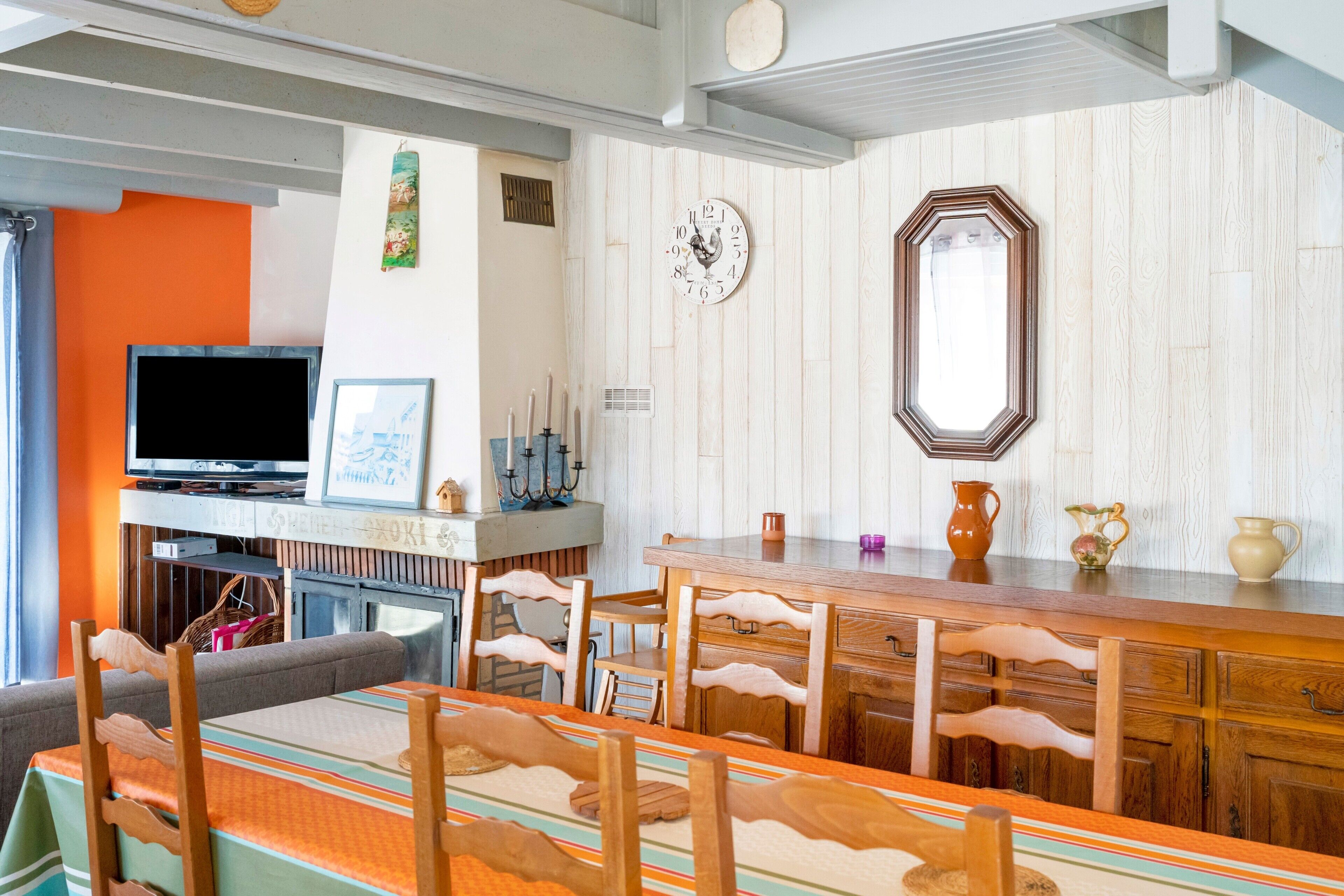 A dining area with a wooden table and chairs, a television, and a clock on the wall.