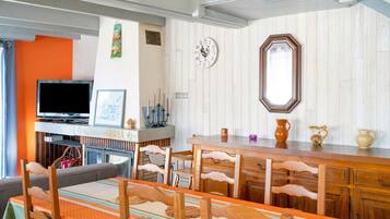 A dining area with a wooden table and chairs, a television, and a clock on the wall.