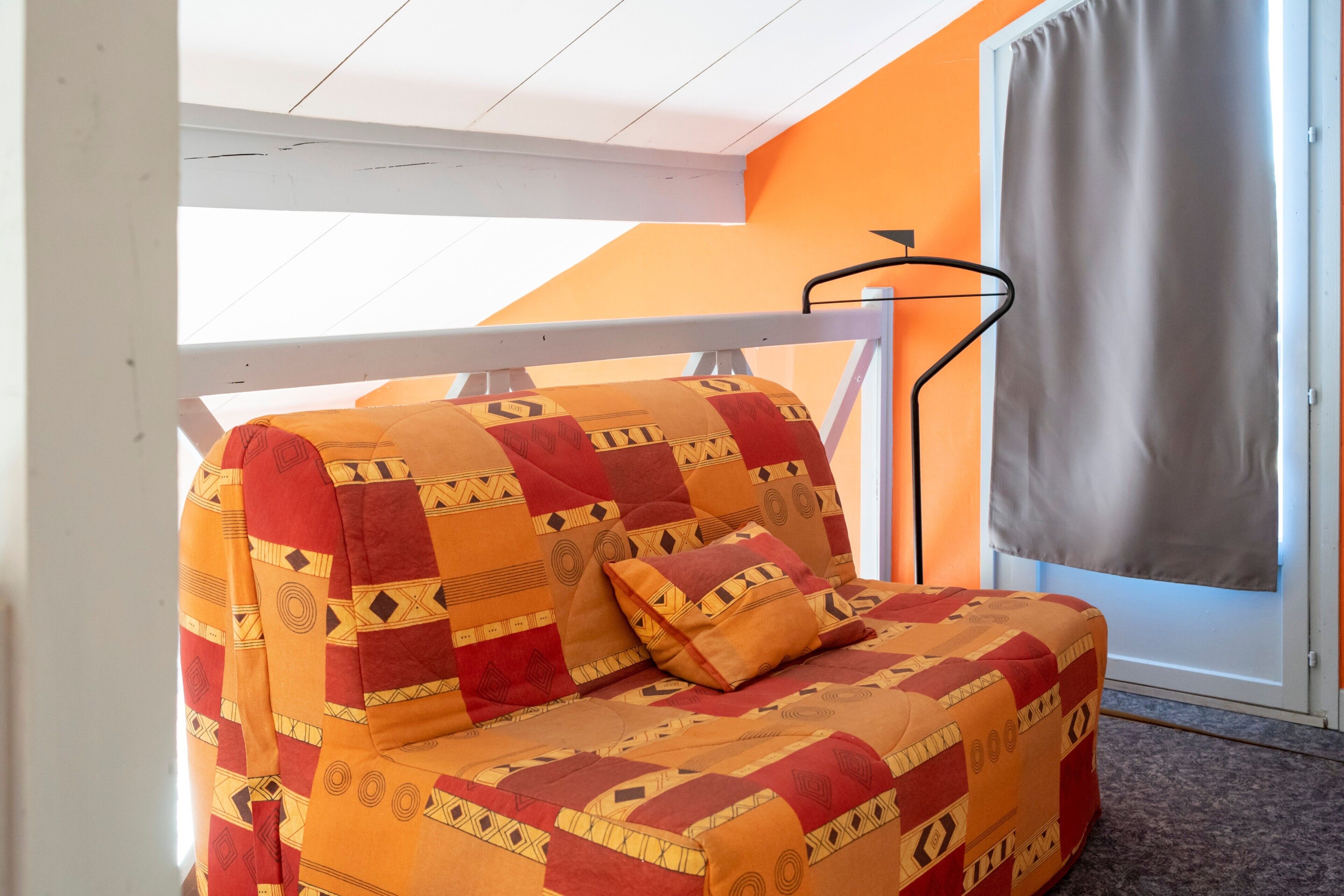 A room with a sofa bed, a window with a curtain, and a ceiling fan.