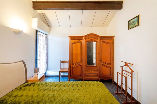 A bedroom with a bed, a wooden wardrobe, a chair, and a hanging rack.