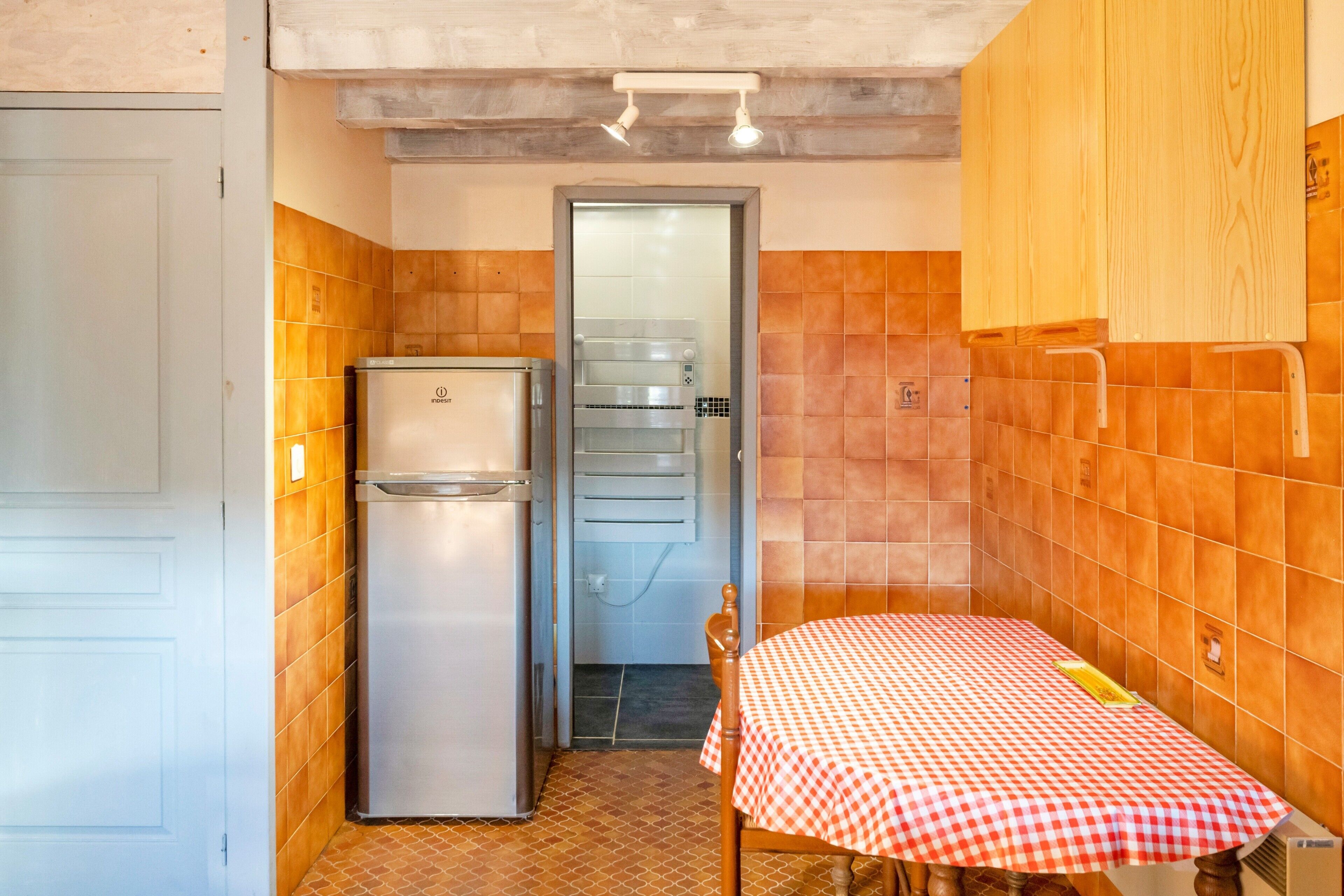 Cocina compacta con refrigerador, horno y una mesa con mantel a cuadros.