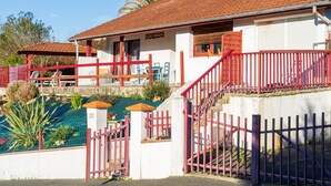 Um edifício de dois andares com um portão vermelho, uma área de varanda coberta e uma piscina.