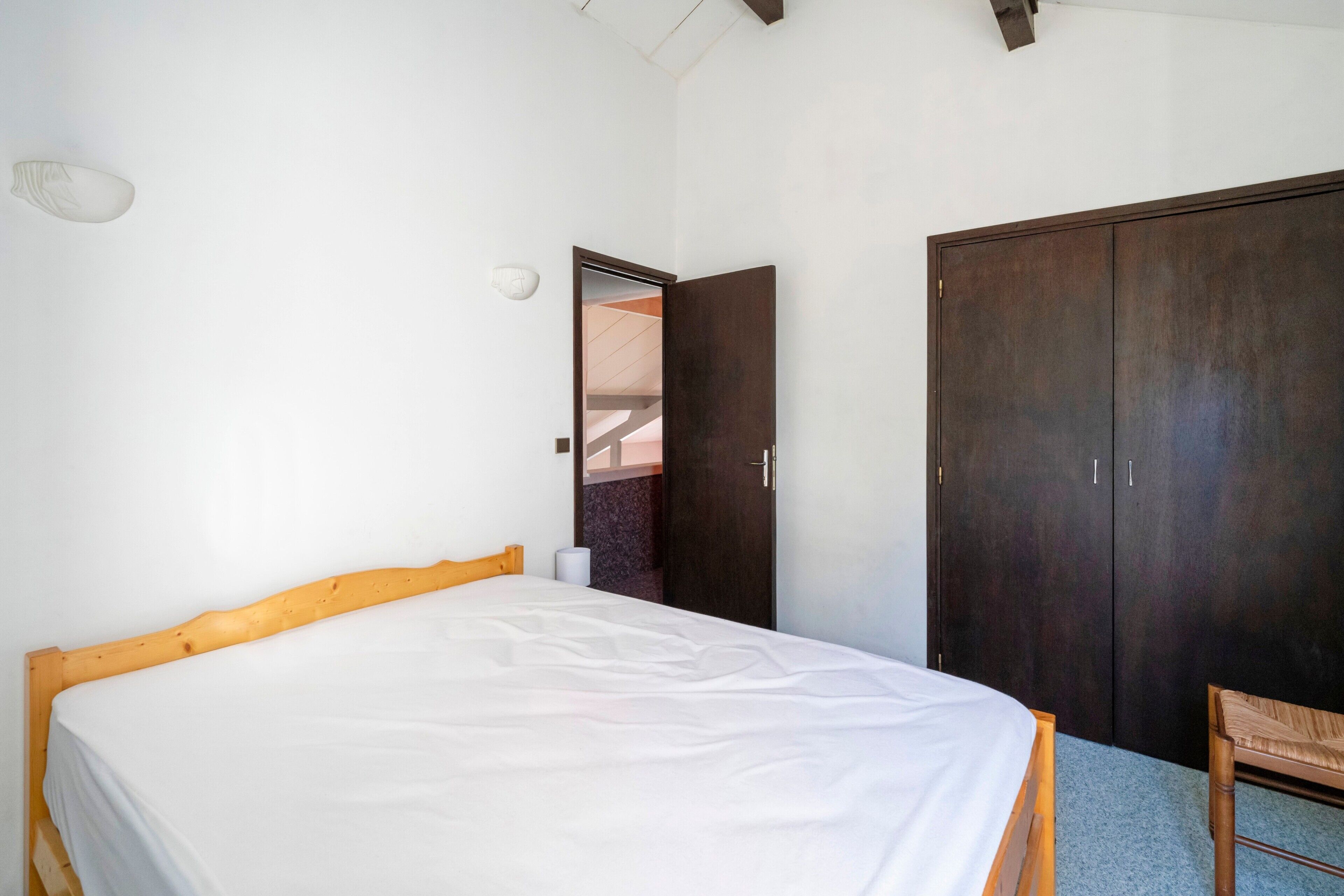 A bedroom with a wooden bed, a dark wardrobe, and a small chair.