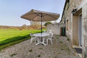 A patio with a round table and chairs, an umbrella, and a stone wall.