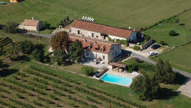 Vue aérienne d’un vaste domaine comprenant une piscine, un vignoble et plusieurs bâtiments.