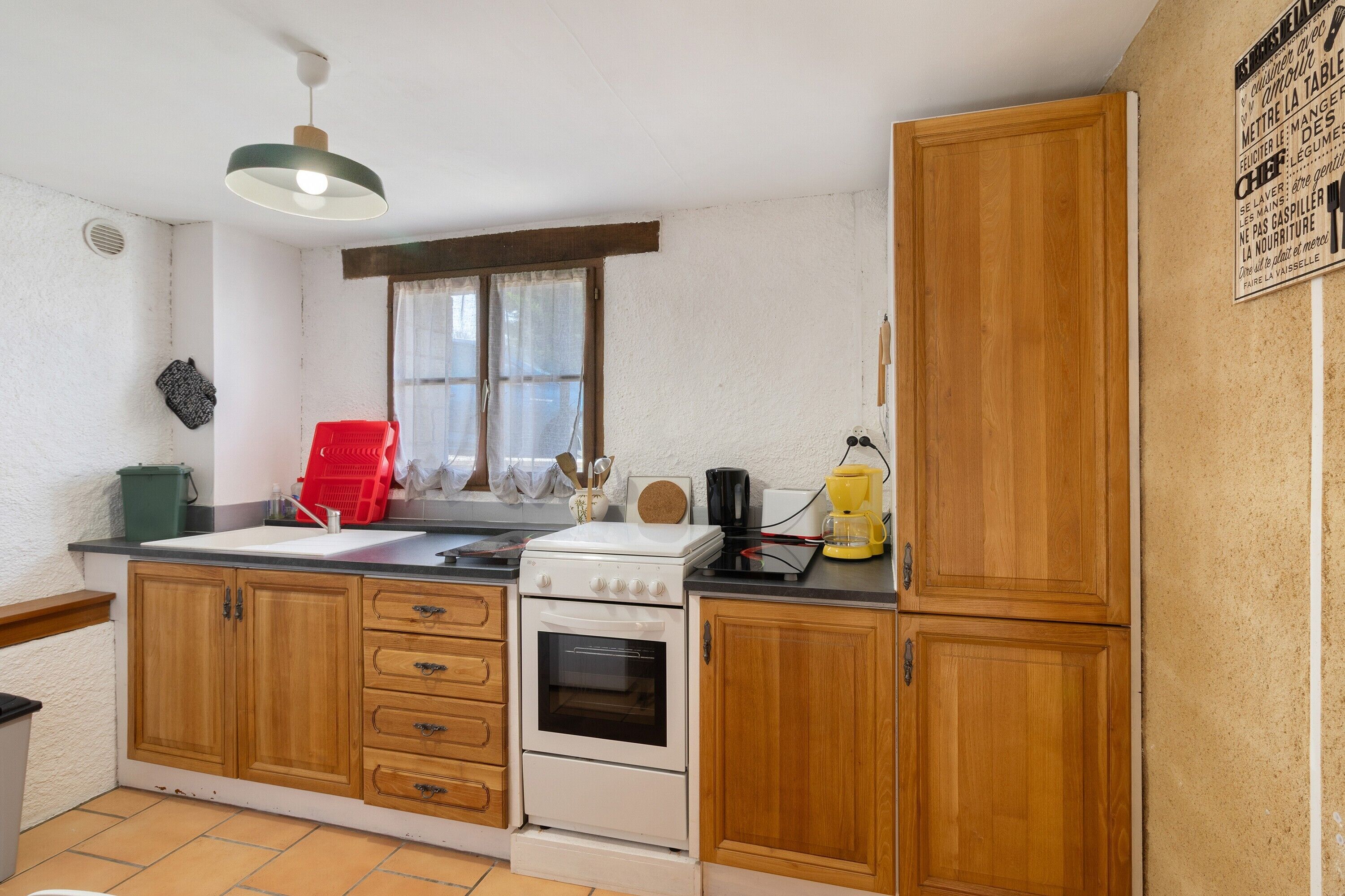 A kitchen with wooden cabinets, a white stove, a window with curtains, and a hanging light fixture.