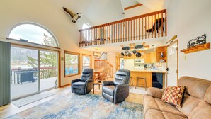 A spacious living room with a large window, a fireplace, and a cozy seating area. - Wake up to Lake Pend Oreille views, soak in the private hot tub, and paddle out from your dock. This lakefront Bayview cabin sleeps 10 with two decks, paddle boards, fire pit, barbeque, and covered boat slip. A unique family getaway in North Idaho! (Bayview)