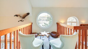 A room with a wooden staircase, a round window with a view, two leather poufs, and a mounted bird. - Wake up to Lake Pend Oreille views, soak in the private hot tub, and paddle out from your dock. This lakefront Bayview cabin sleeps 10 with two decks, paddle boards, fire pit, barbeque, and covered boat slip. A unique family getaway in North Idaho! (Bayview)