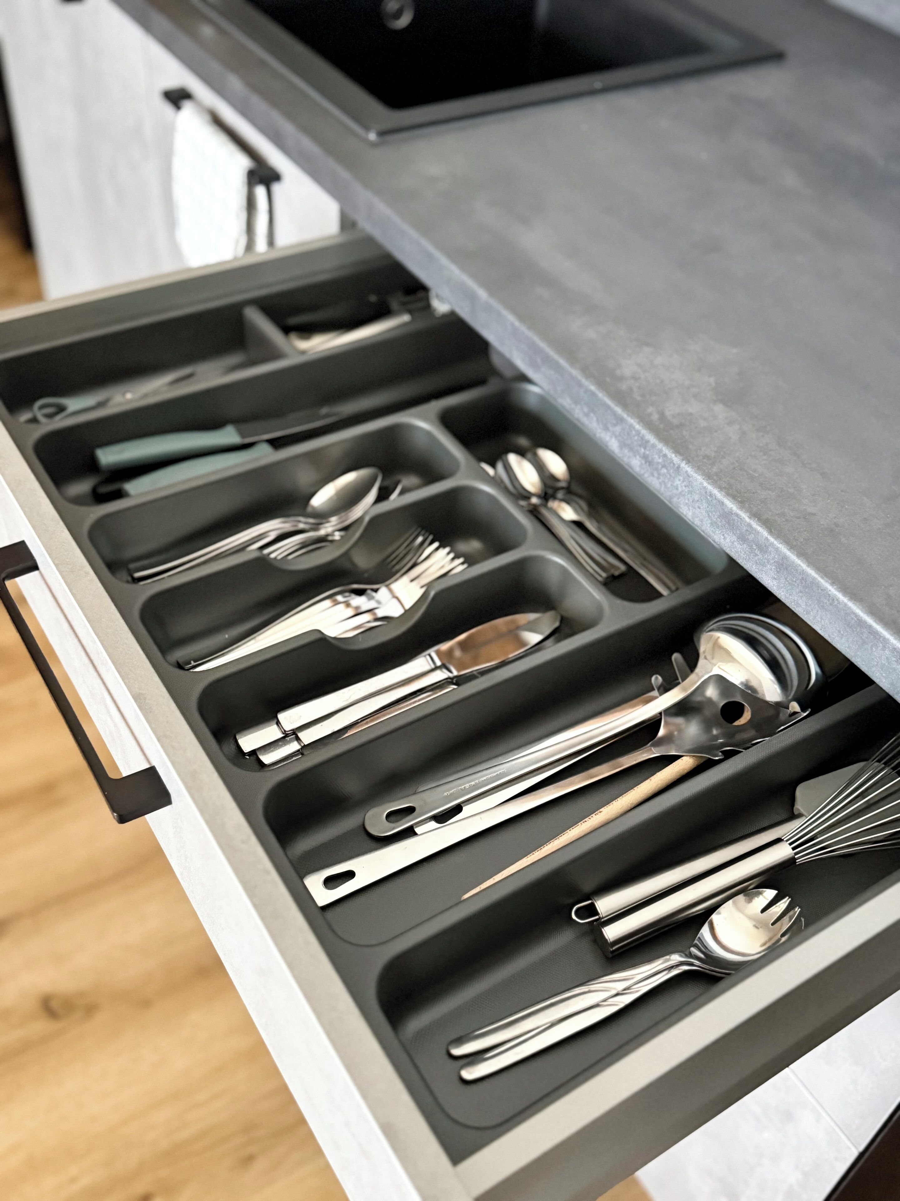 A kitchen drawer with utensils organized in compartments.