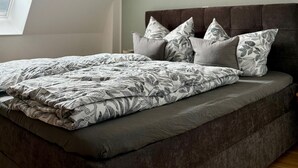 Un dormitorio con techo inclinado, una cama con colcha estampada y tres cuadros colgados en la pared.