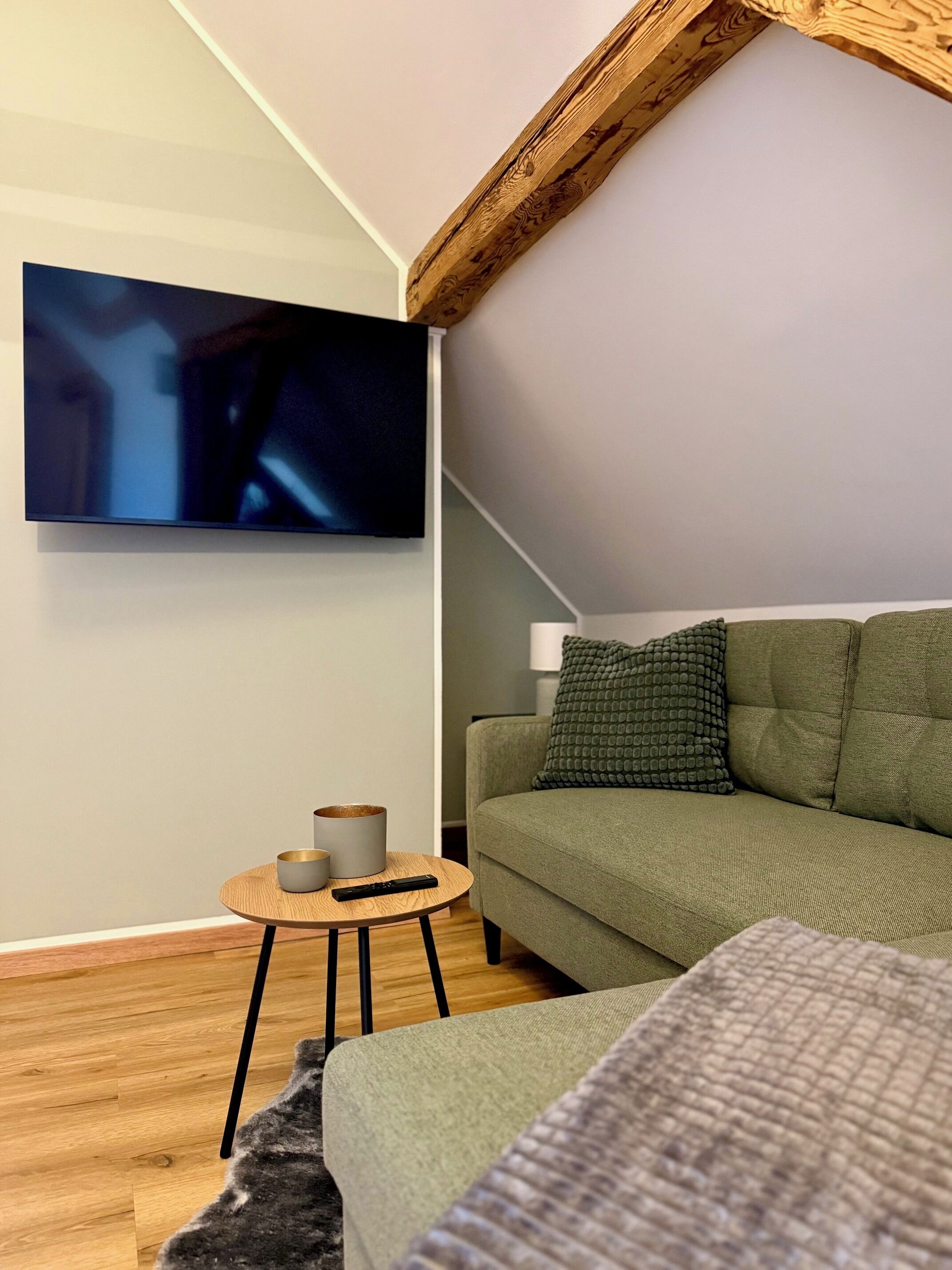 A modern living room with a green sofa, a round wooden coffee table, and a flat-screen TV mounted on the wall.