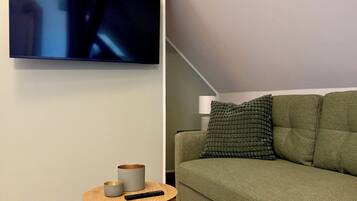 A modern living room with a green sofa, a round wooden coffee table, and a flat-screen TV mounted on the wall.