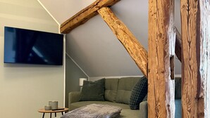 Un dormitorio tipo loft acogedor con vigas de madera a la vista, un sofá gris y un televisor de pantalla plana montado en la pared.