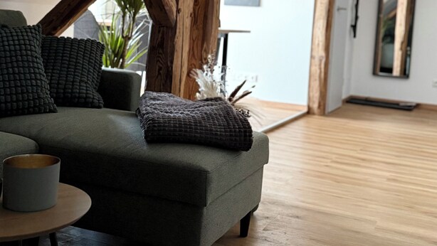 Un moderno loft con vigas de madera expuestas, un sofá verde, una mesita redonda y una planta en maceta.