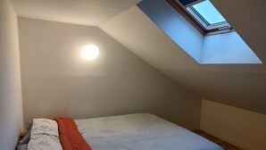 Una piccola camera con un letto singolo, un soffitto spiovente e una finestra a lucernario.