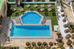 Ein achteckiger Pool mit einer umlaufenden Sonnenterrasse, Liegestühlen und einer kleinen Sitzecke mit Tischen und Sonnenschirmen.