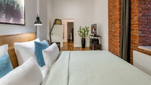 Un dormitorio con cama, almohadas, una lámpara, una planta y una pared de ladrillo.