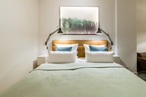 Una cama bien hecha con cabecera, dos lámparas de noche y una ventana con vista a árboles.