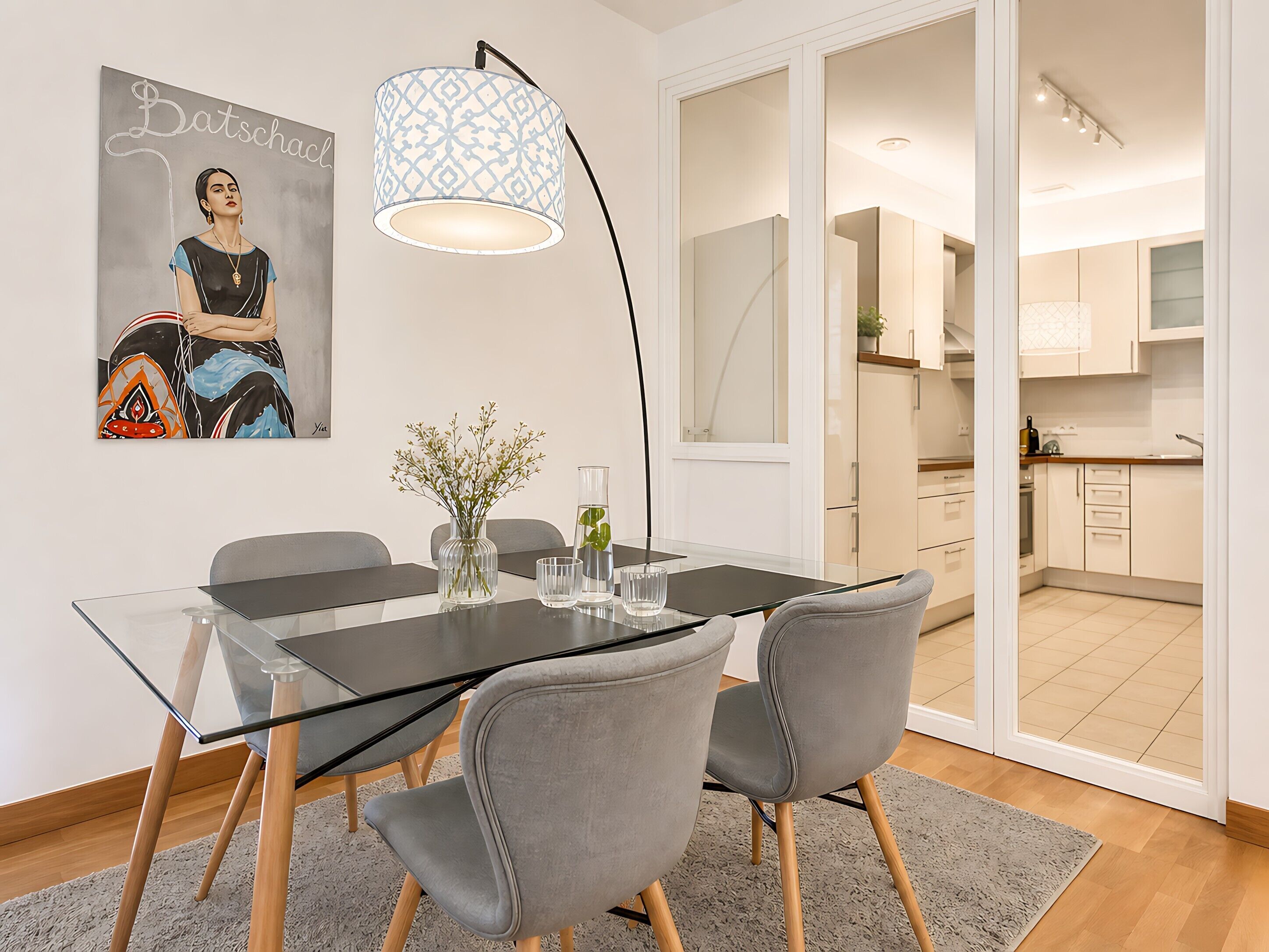 A modern dining area with a glass table, grey chairs, a vase with flowers, and a pendant light.