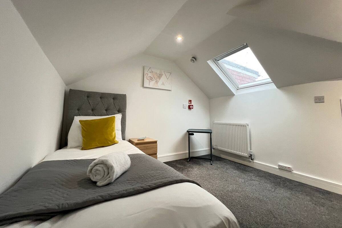A bedroom with a bed, a skylight, a radiator, and a small table.