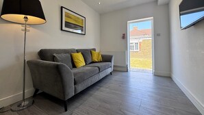Un salon moderne avec un canapé gris, une lampe sur pied et un tableau encadré accroché au mur.