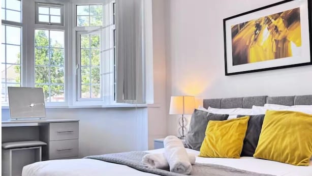 Une chambre d’hôtel avec un lit, un bureau avec un ordinateur portable, une fenêtre avec des rideaux et une lampe fixée au mur.
