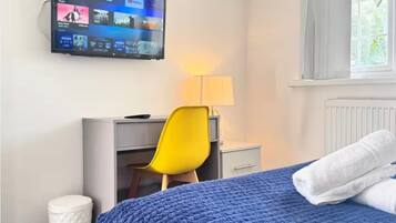 A hotel room with a bed, a desk, a chair, a TV mounted on the wall, and a window with curtains.