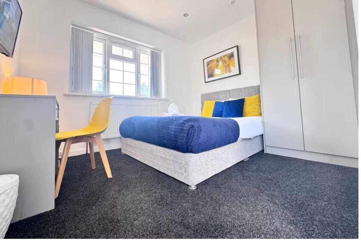 A bedroom with a bed, a chair, a desk, and a wardrobe.